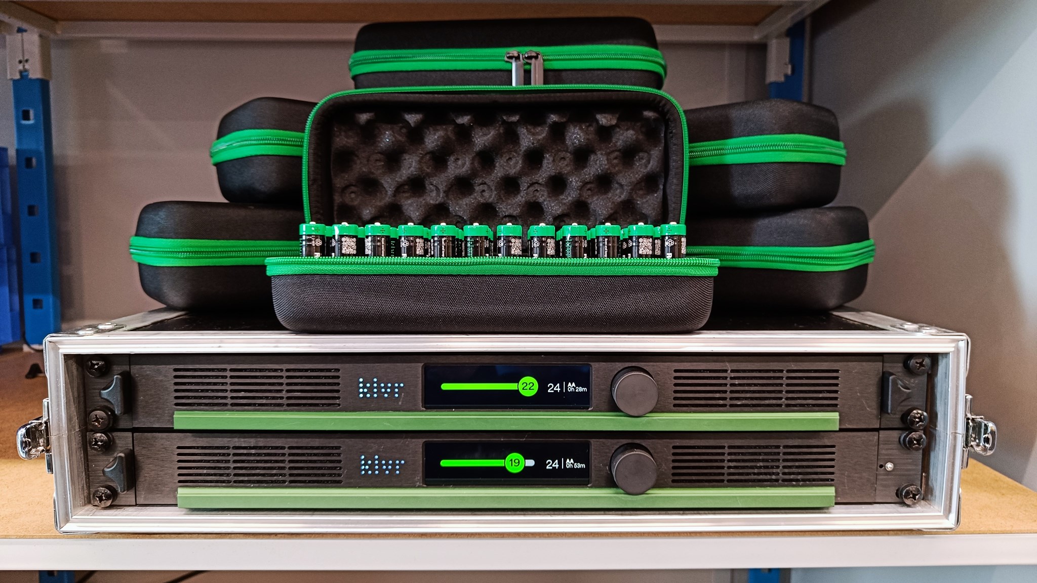 Twee batterijladers in een rack gemonteerd met tasjes gevuld met batterijen er bovenop.